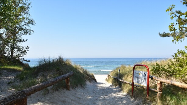 En sti af sand der fører hen til havet, med et skilt der angiver et område med klitbeskyttelse.