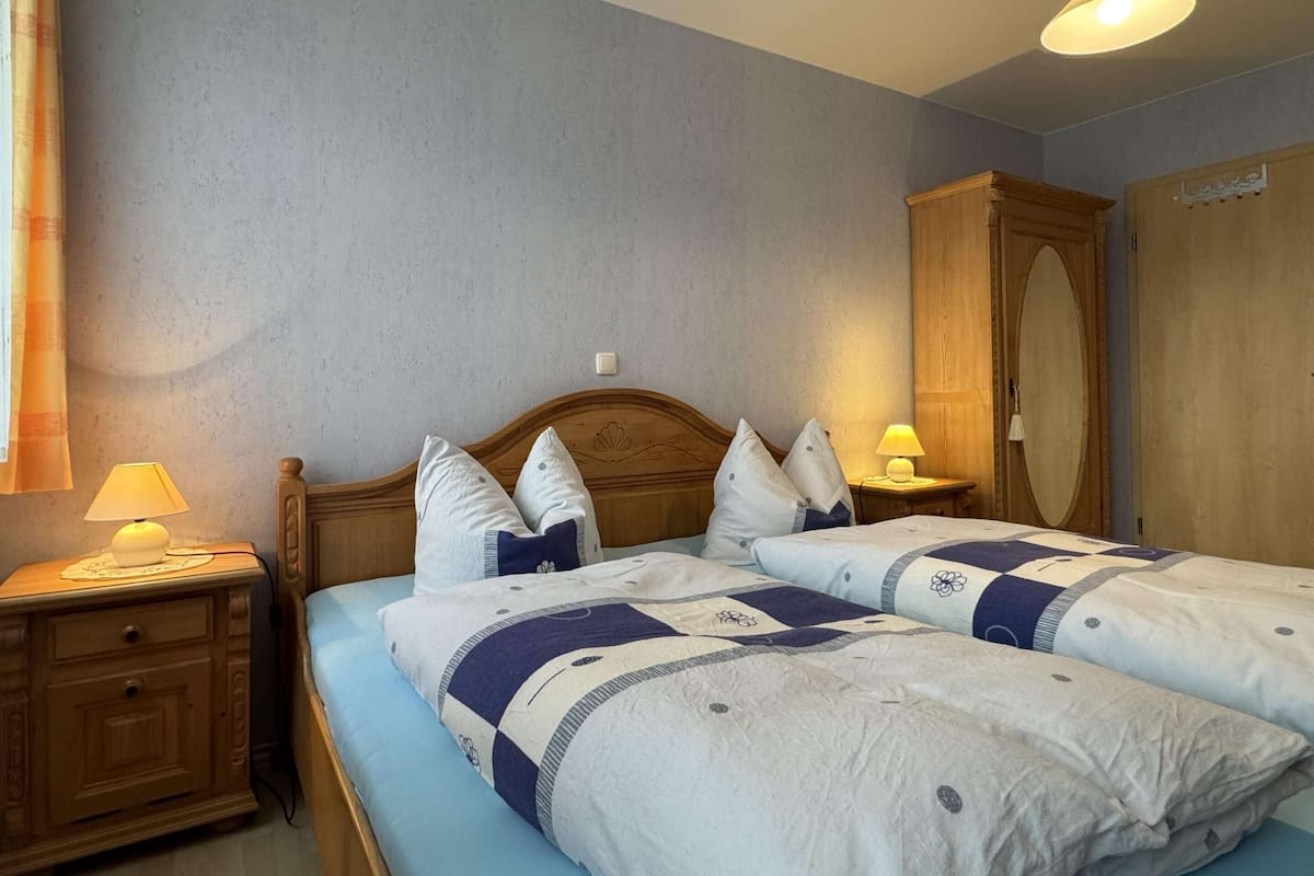 Quarto com duas camas, cabeceiras de madeira, luminárias de cabeceira e um guarda-roupa.