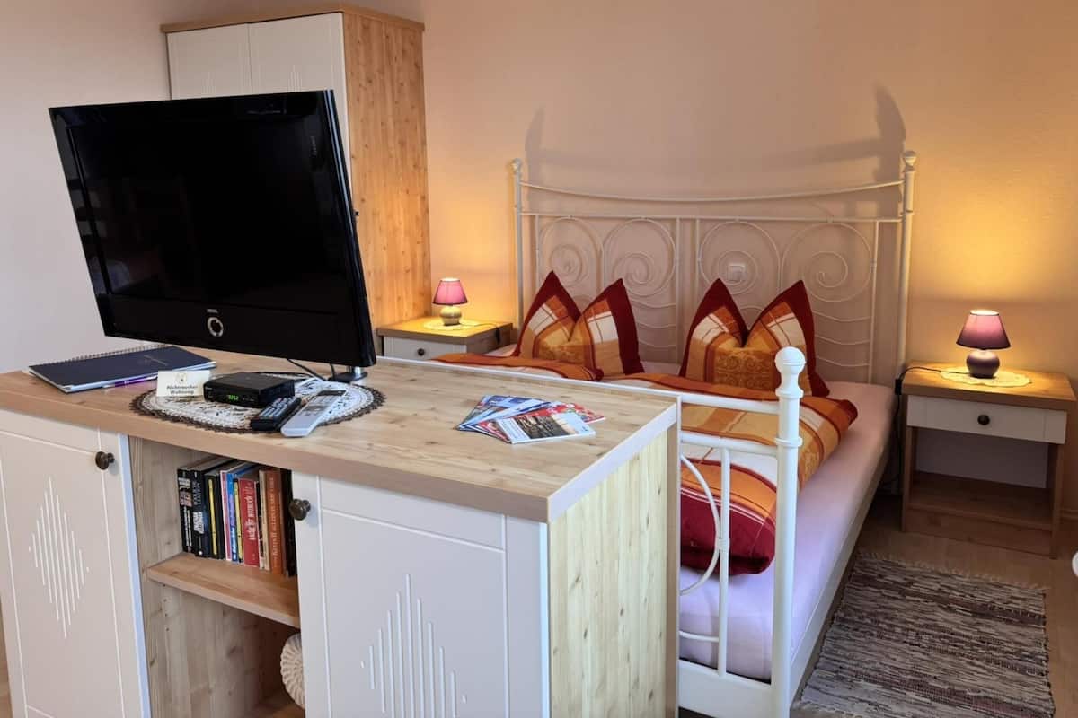 A bedroom with a bed, bedside lamps, a TV, a desk with books, and a wardrobe.