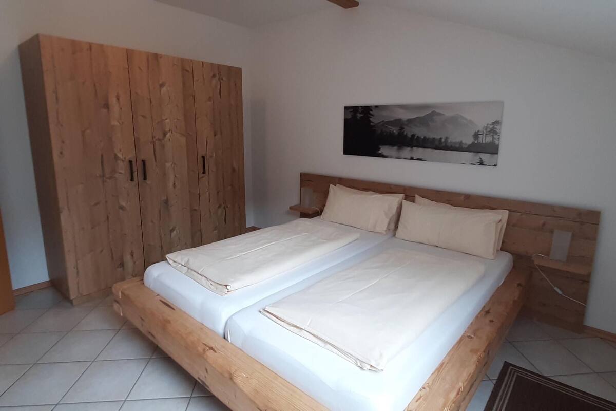 Un dormitorio con una cama de madera, un armario y un cuadro de un paisaje montañoso en la pared.