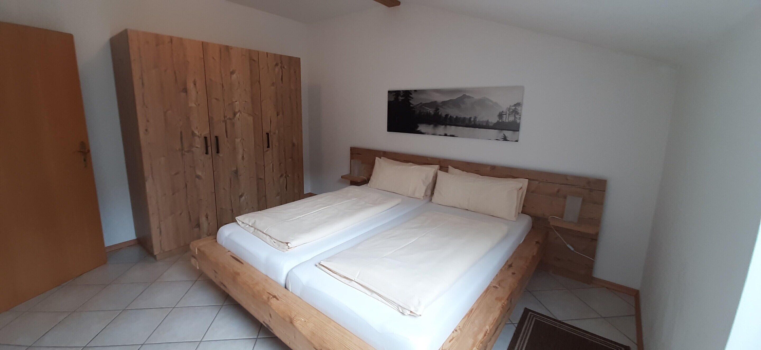 A bedroom with a wooden bed, a wardrobe, and a wall-mounted picture.