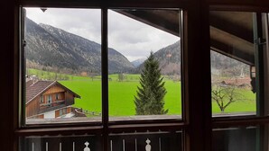 A view from a window with a wooden frame, overlooking a green field and a mountain range. - Lush Apartment in Bayrischzell With 2 Saunas (Bayrischzell)