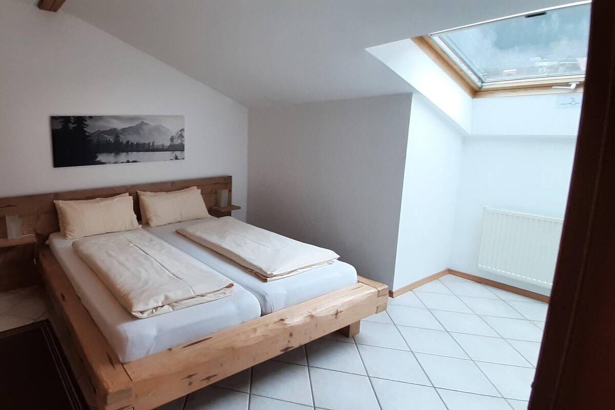 A bedroom with a wooden bed, a skylight, a white radiator, and a mountain landscape painting on the wall.