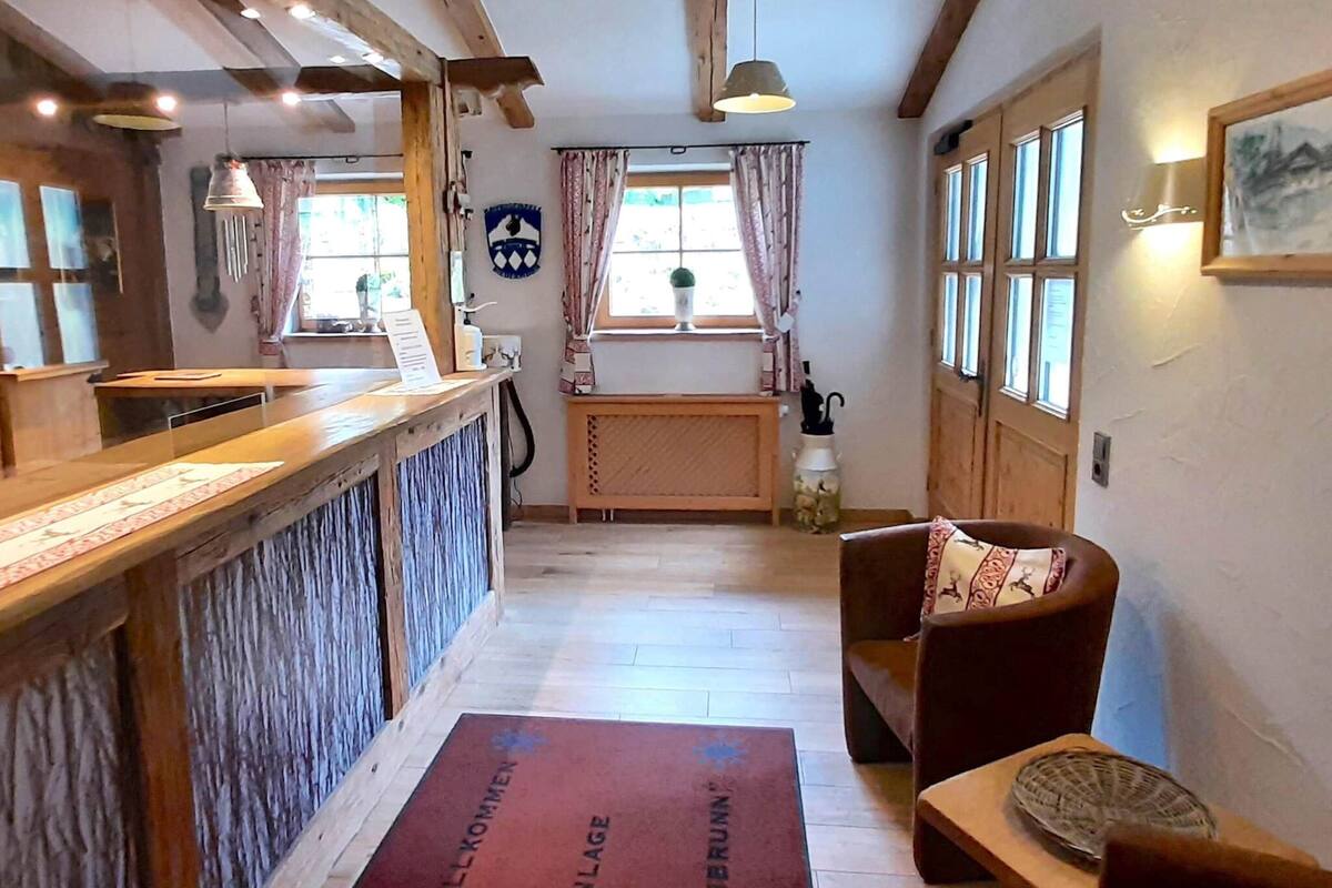 Un espace d’accueil comprenant un comptoir en bois, un bureau d’accueil, une chaise avec un coussin, une fenêtre avec des rideaux et une porte.