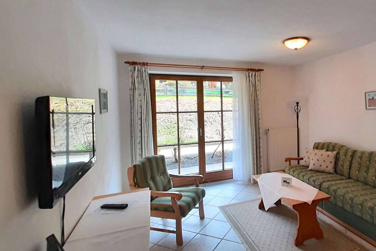 A living room with a sofa, a chair, a table, a TV, and a window with curtains.