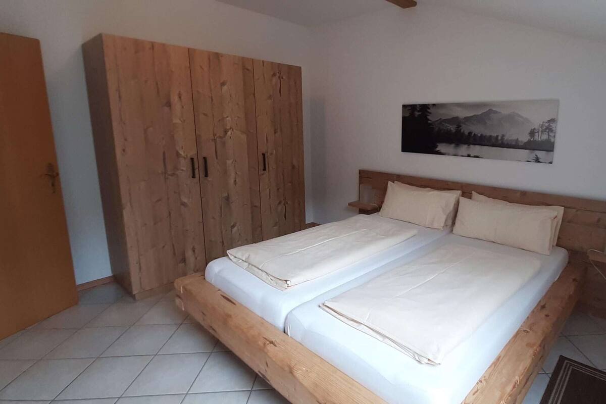 Un dormitorio con cama de madera, un armario grande y una pintura de un paisaje montañoso en la pared.