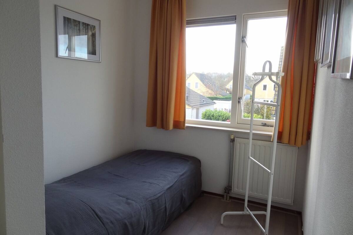 Une petite chambre avec un lit simple, une fenêtre, un radiateur et un tableau au mur.