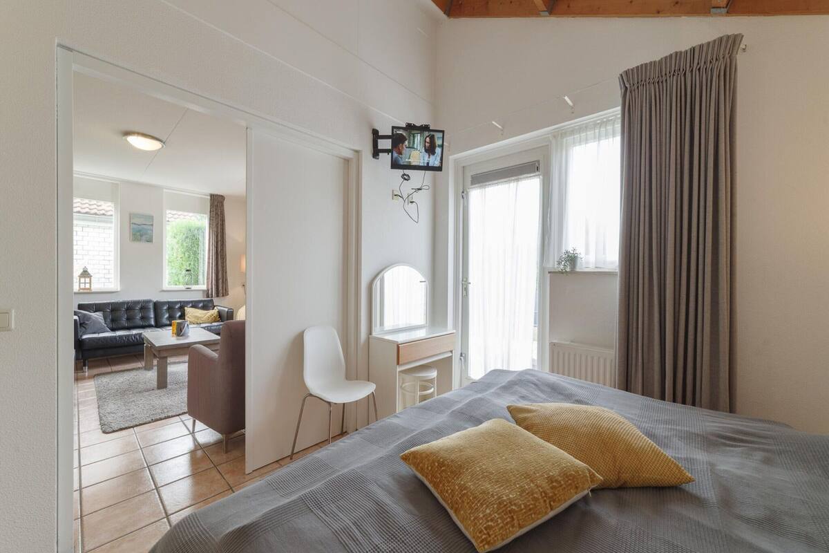 Une chambre à coucher comprenant un lit, deux oreillers, un bureau, une chaise et un téléviseur fixé au mur.