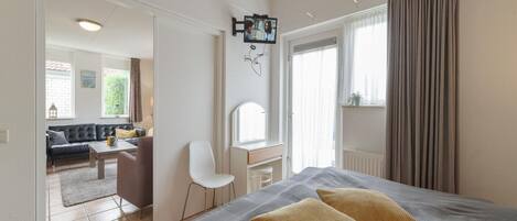 A bedroom with a bed, two pillows, a desk, a chair, and a television mounted on the wall.