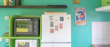 A kitchen with a green wall, a white refrigerator, a black microwave, and a white oven. There are various kitchen items and decorations on the wall.