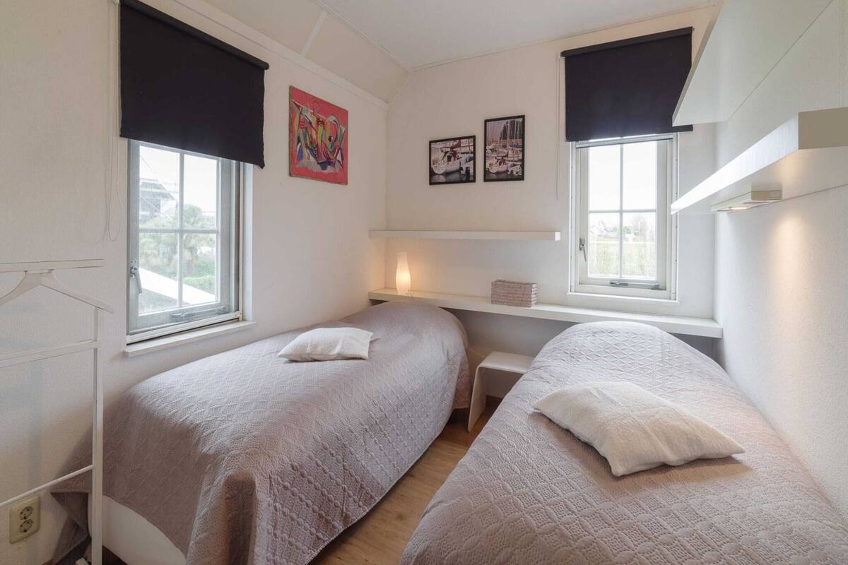 Une chambre avec deux lits, une fenêtre et une étagère où sont posées des photos.