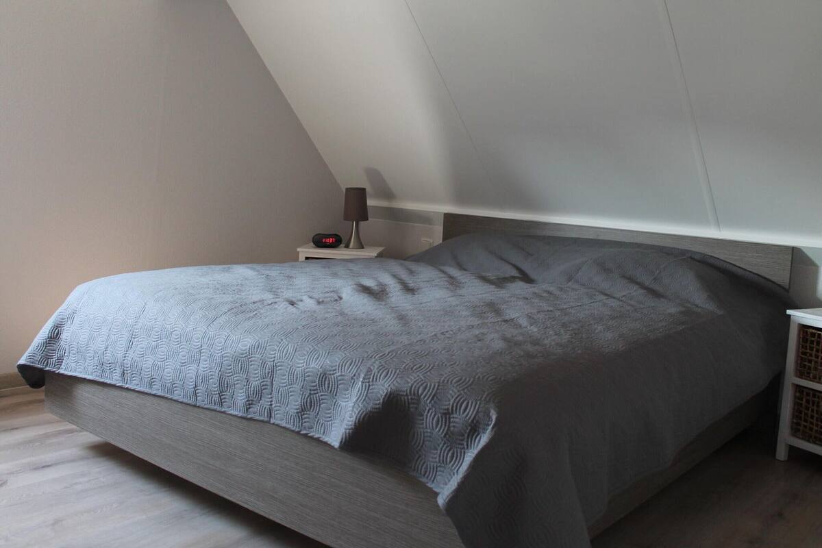 Une chambre à coucher avec un lit, une table de chevet, une lampe et une horloge numérique.