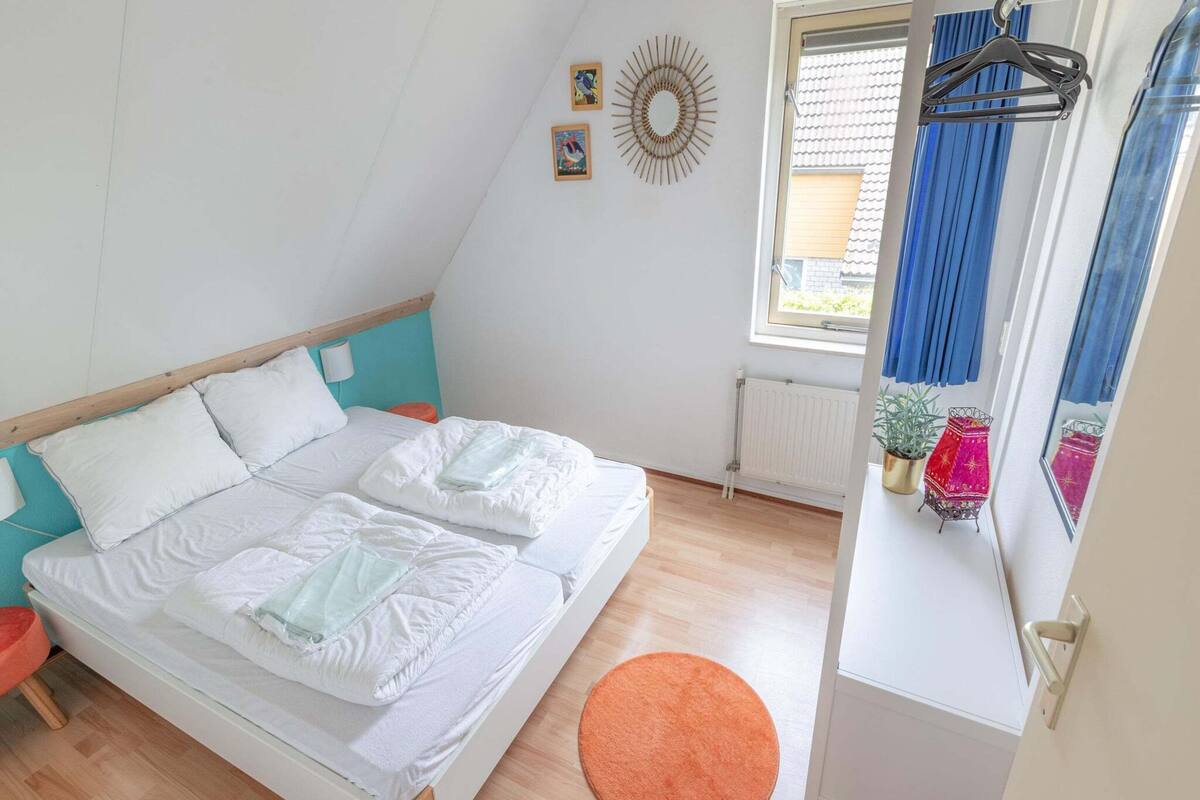 Une chambre à coucher avec un lit, une fenêtre avec des rideaux, un radiateur et un petit tapis orange.