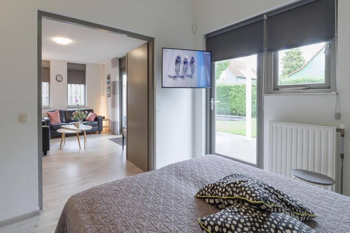 Une chambre à coucher avec un lit, un téléviseur fixé au mur et une vue sur l’extérieur par une fenêtre.