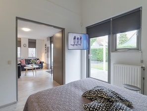 A bedroom with a bed, a TV mounted on the wall, and a view of the outside through a window. - Nice Holiday Home With Washing Machine, in a Holiday Park 200m. From the Beach (Wemeldinge)