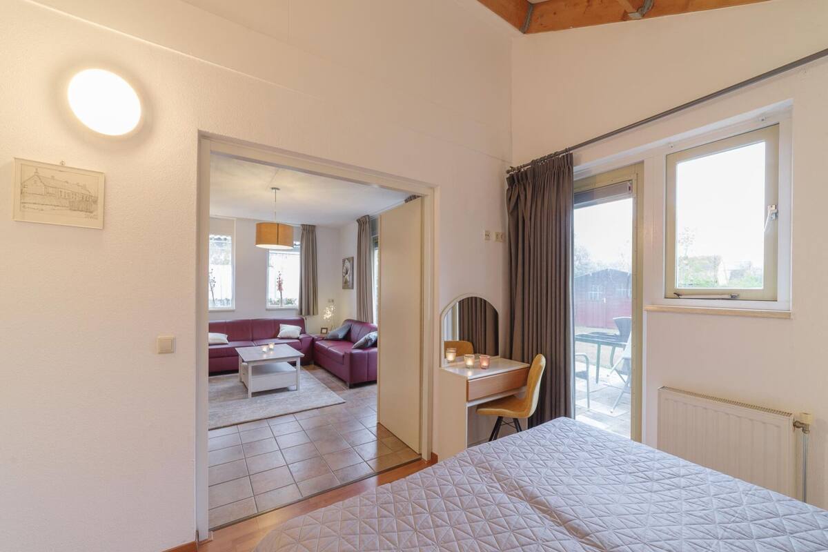 Une chambre à coucher avec un lit, un bureau et une chaise. Il y a une fenêtre avec des rideaux et une vue sur l’extérieur.