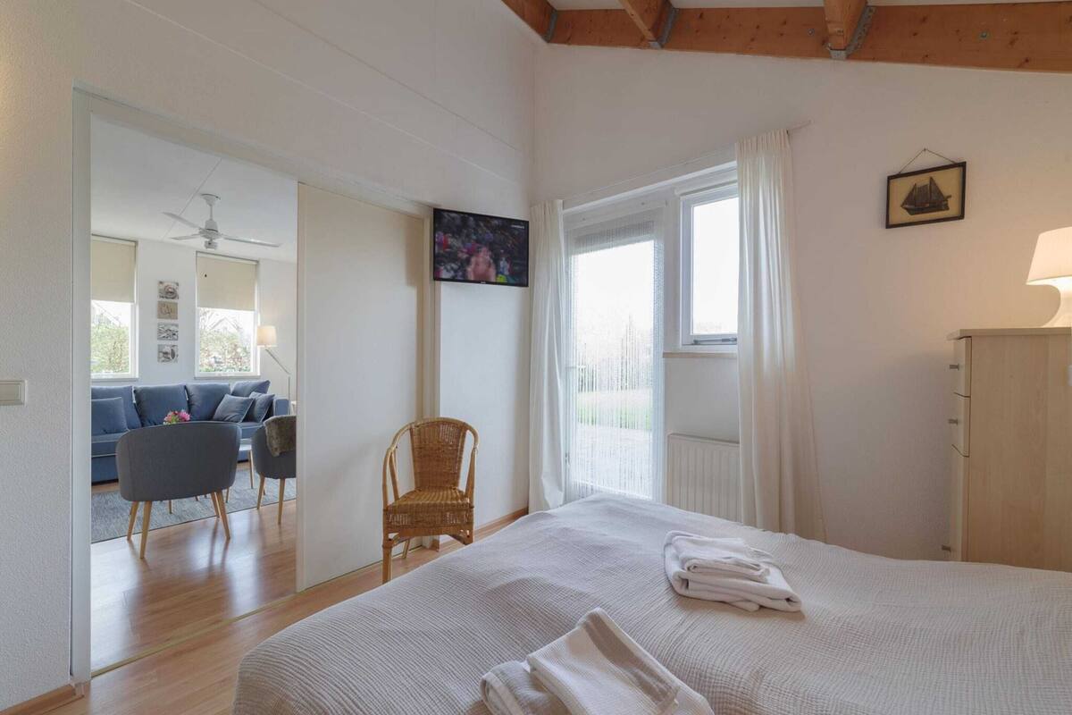 Une chambre avec un grand lit, une chaise, une commode et une vue sur un espace de vie comprenant un canapé et un téléviseur.