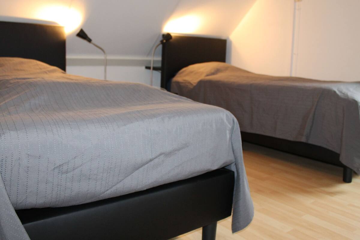 Une chambre avec deux lits, un plancher en bois et un mur blanc.