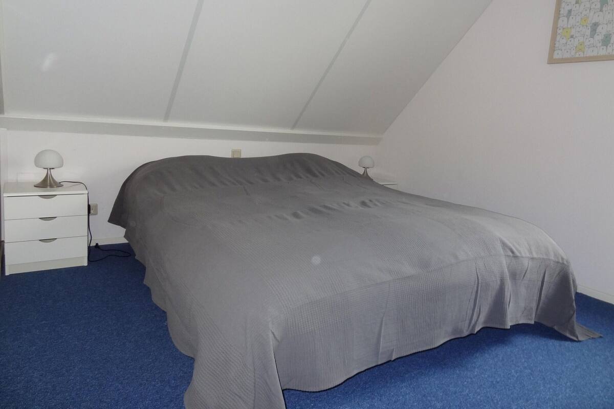 Une chambre avec un lit simple, une table de chevet et une lampe fixée au mur.