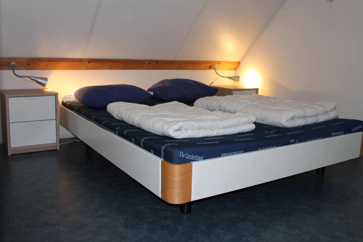 Un lit simple avec un matelas bleu et du linge de lit blanc, deux tables de chevet avec des lampes et une tête de lit en bois.