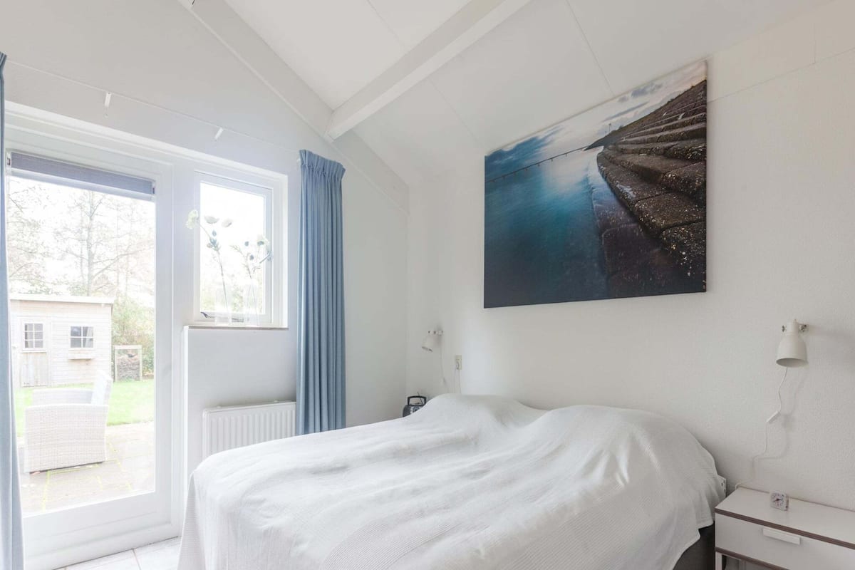 Une chambre à coucher avec un lit, une fenêtre avec des rideaux, une table de chevet et un tableau accroché au mur.