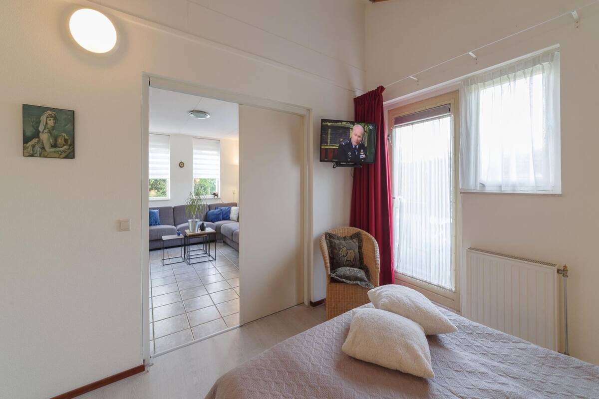 Une chambre avec un lit, une télévision, une chaise et une vue sur le salon.