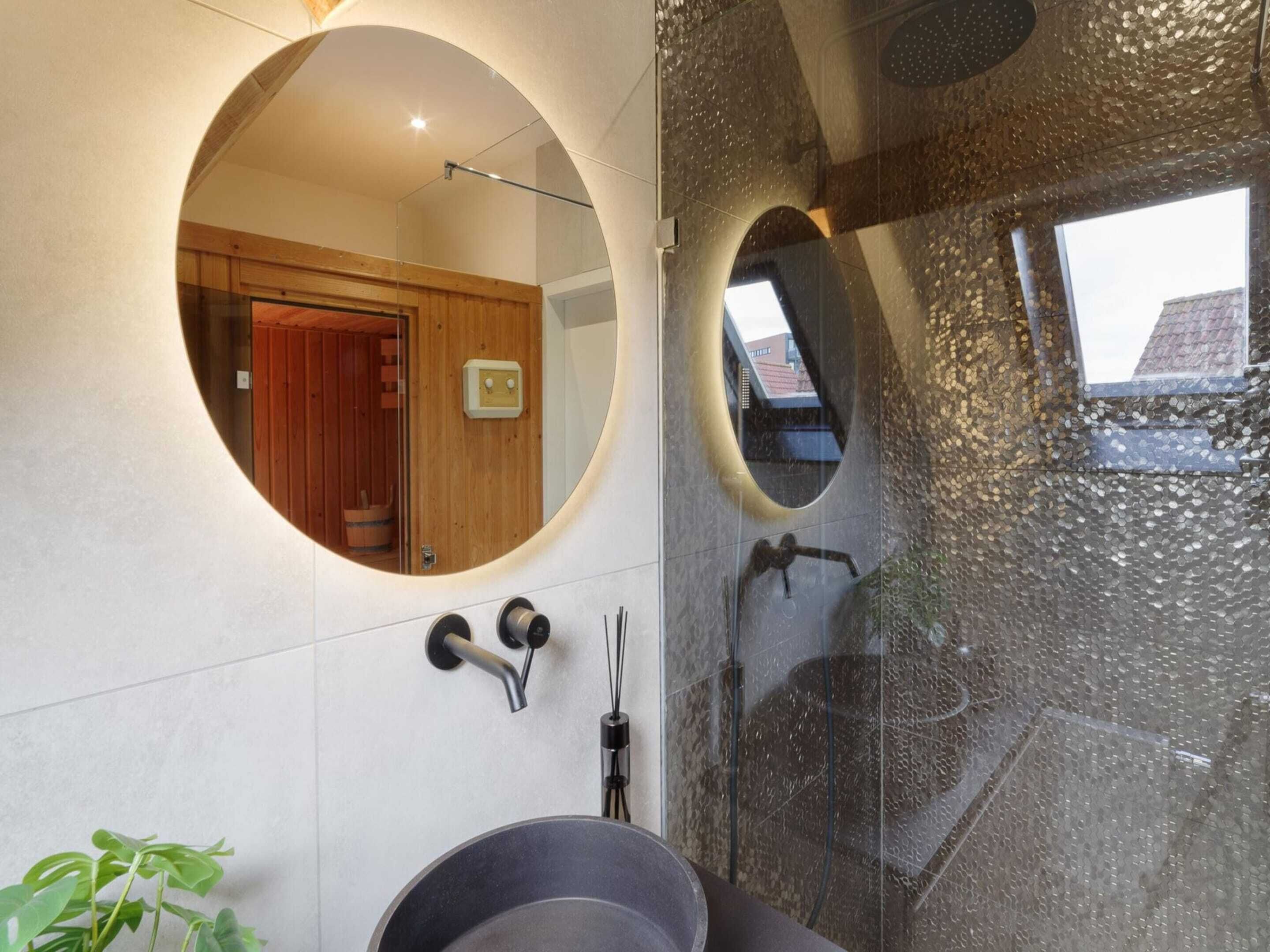 A modern bathroom with a circular mirror, a shower with a textured wall, and a visible wooden door.