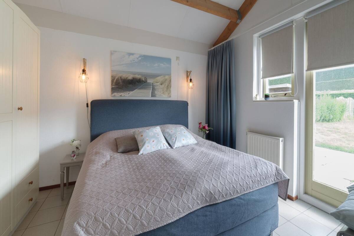 Une chambre à coucher avec un grand lit, une table de chevet, un tableau et une fenêtre avec des rideaux.