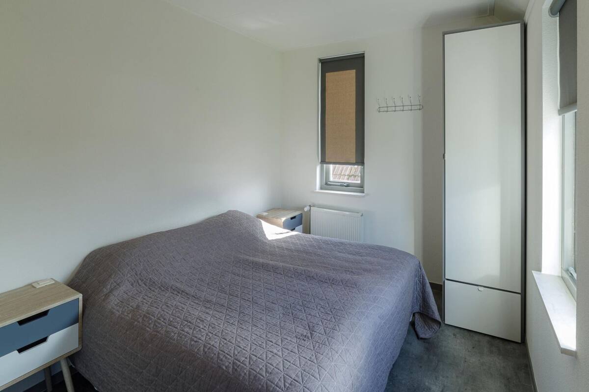 Une chambre à coucher comprenant un lit, une table de chevet, un radiateur, une fenêtre et une armoire.