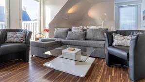 A modern living room with a grey sectional sofa, two black armchairs, a glass coffee table, and a white accent piece. - Comfortable Holiday Apartment in St. Peter Ording (St. Peter-Ording)
