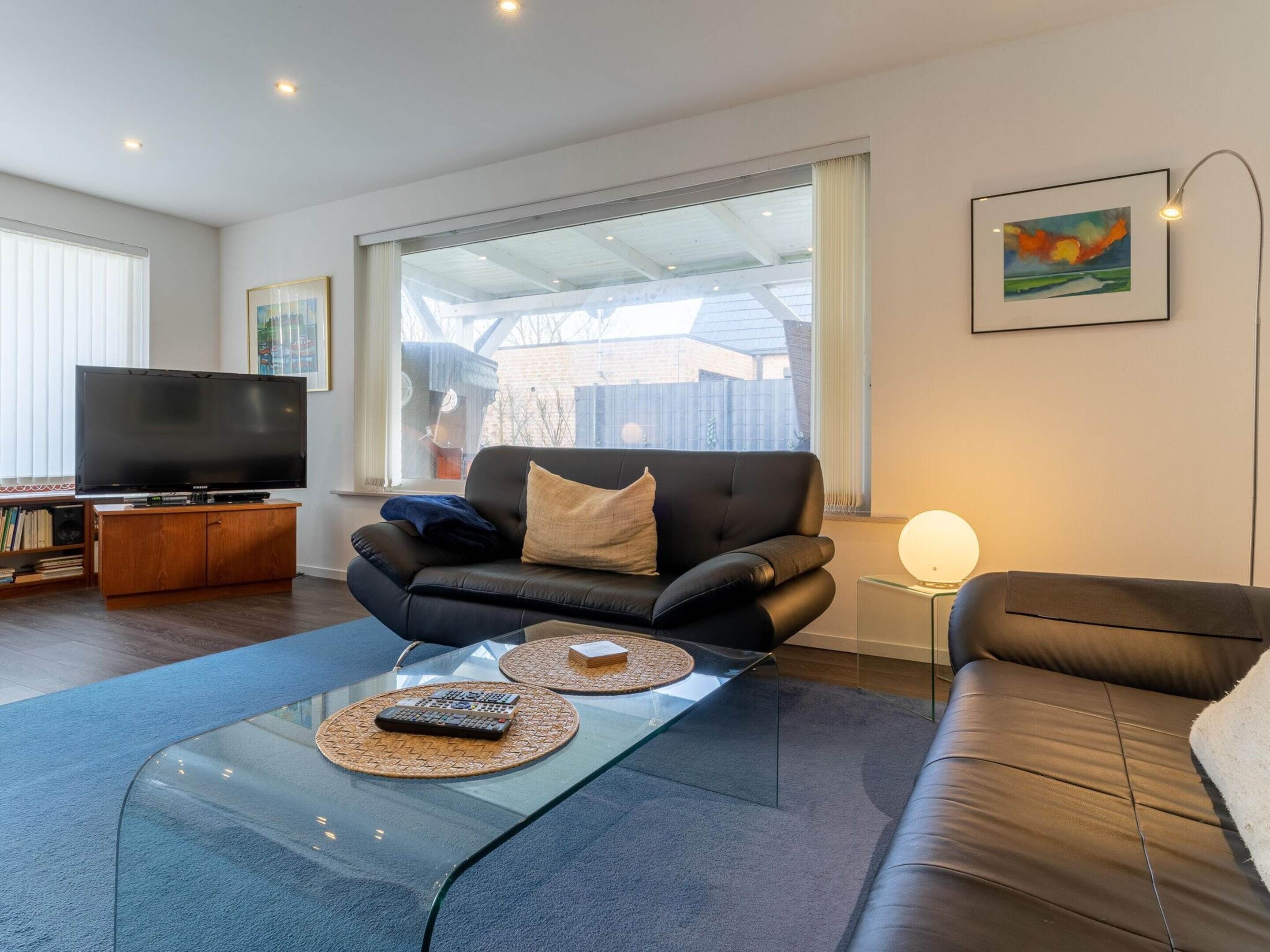 A modern living room with a leather sofa, a glass coffee table, and a flat-screen TV.