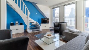 A modern living room with a blue accent wall, a staircase, a flat-screen TV, a glass coffee table, and a sofa. - Comfortable Holiday Apartment in St. Peter Ording (St. Peter-Ording)