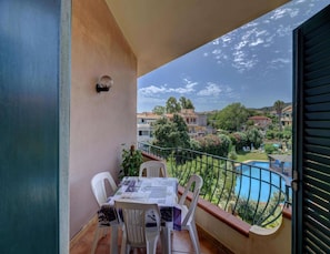 Un balcon avec une table et des chaises, une piscine et une vue sur les bâtiments et la verdure.