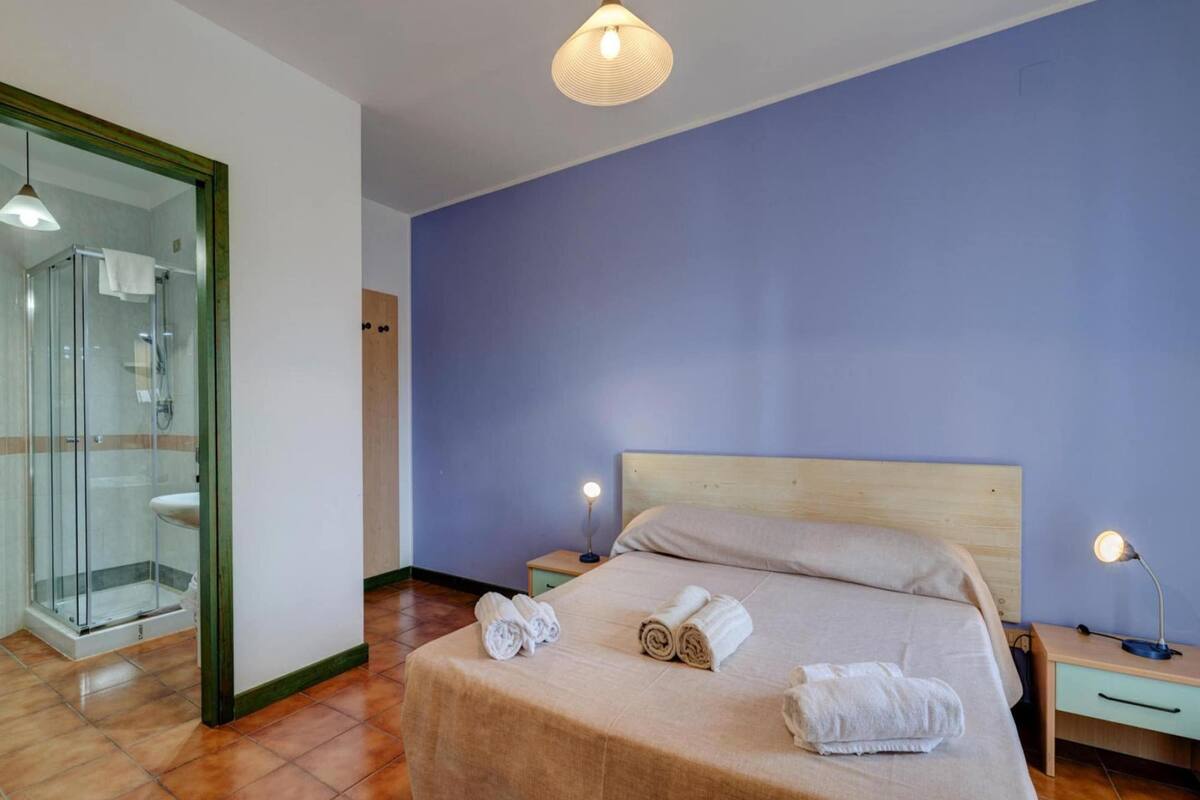 Ein Schlafzimmer mit einem Bett, zwei Nachttischen, einer Ablage und einer Duschkabine aus Glas, sowie einer Holztür.