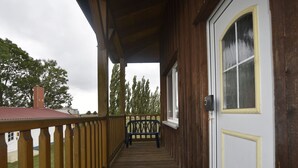 Un portico in legno con una panchina, una porta con un numero e vista sugli alberi.