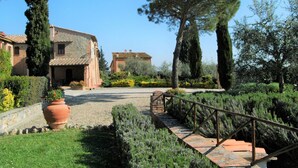 A traditional stone building with a tiled roof, surrounded by well-maintained gardens and a gravel pathway leading to a wooden bridge. - Flat With Shared Pool and air Conditioning (Castelfiorentino)