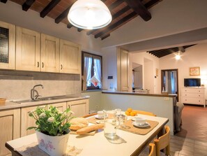 A modern kitchen with wooden cabinets, a sink, and a dining area with a table set for two. - Flat With Shared Pool and air Conditioning (Castelfiorentino)