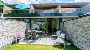 A modern house with a stone exterior, a wooden deck, and a glass door leading to an indoor area. - Modern Apartment With Balcony and Access to Sauna (Neukirchen am Grossvenediger)
