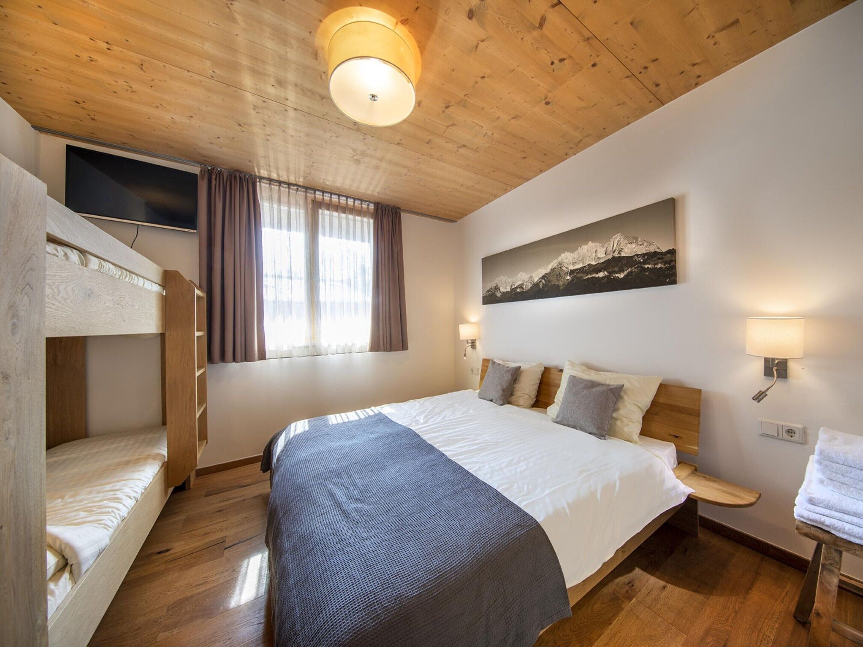 A bedroom with a bunk bed, a large bed, a painting, and a TV on the wall.