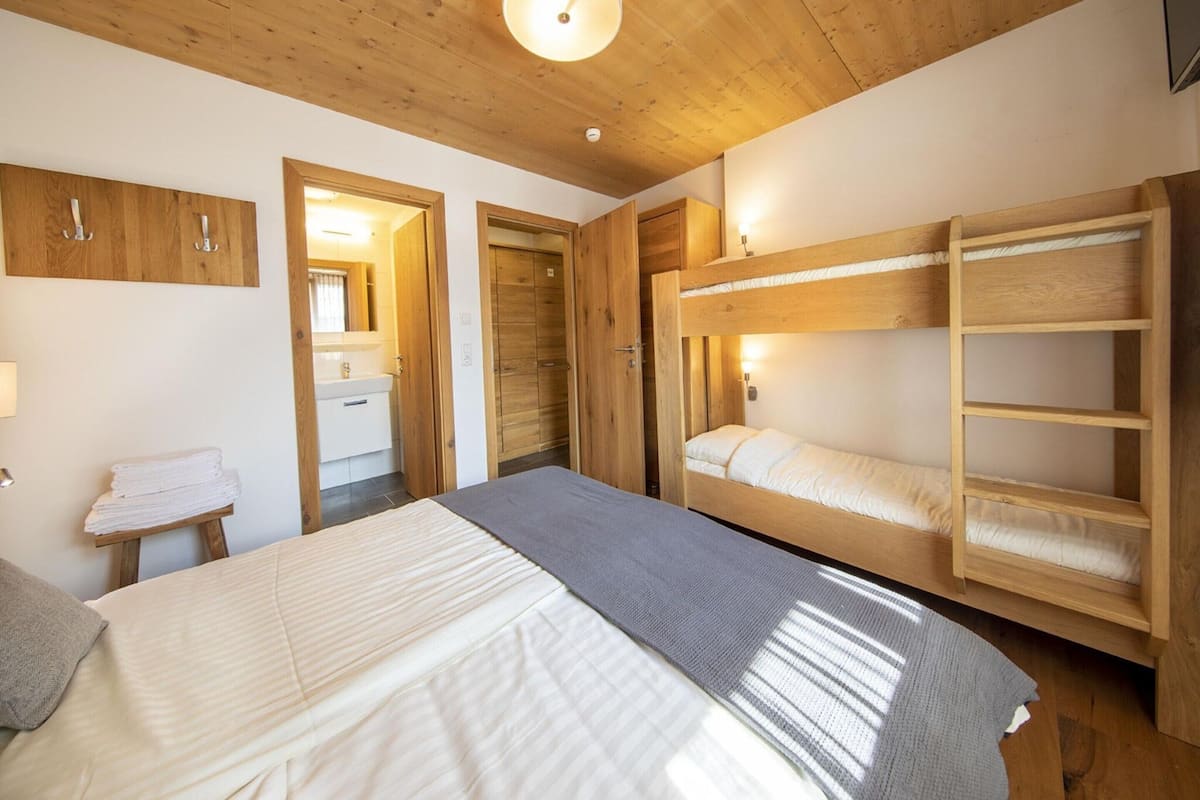A bedroom with a bunk bed, a bedside table, a mirror, and wooden doors.
