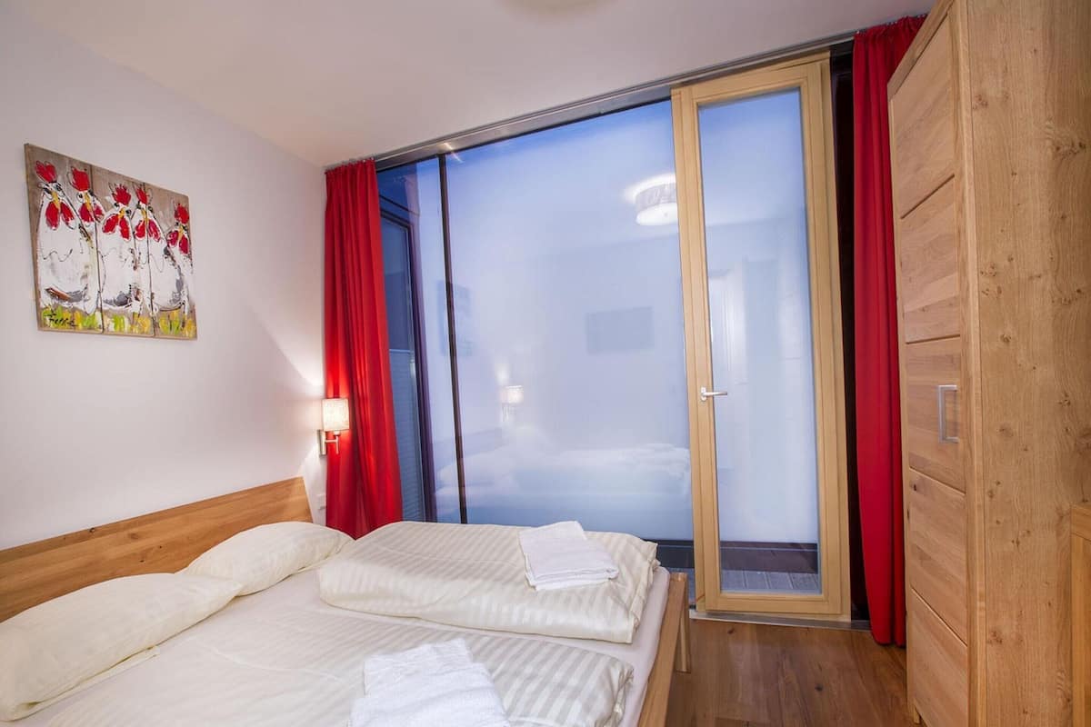 A hotel room with two beds, a wooden wardrobe, a sliding glass door to the balcony, and a painting on the wall.
