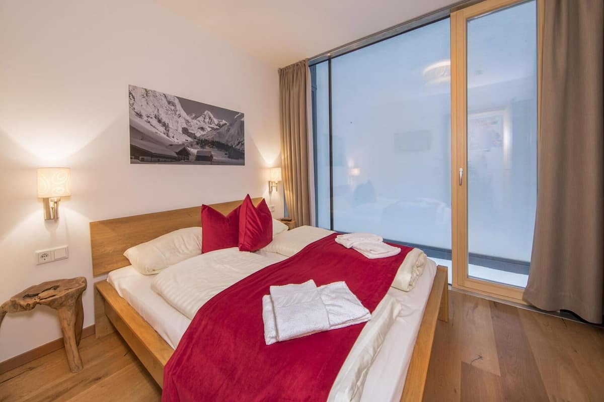 A bedroom with a large bed, a wooden headboard, a red throw blanket, and a mountain landscape painting on the wall.