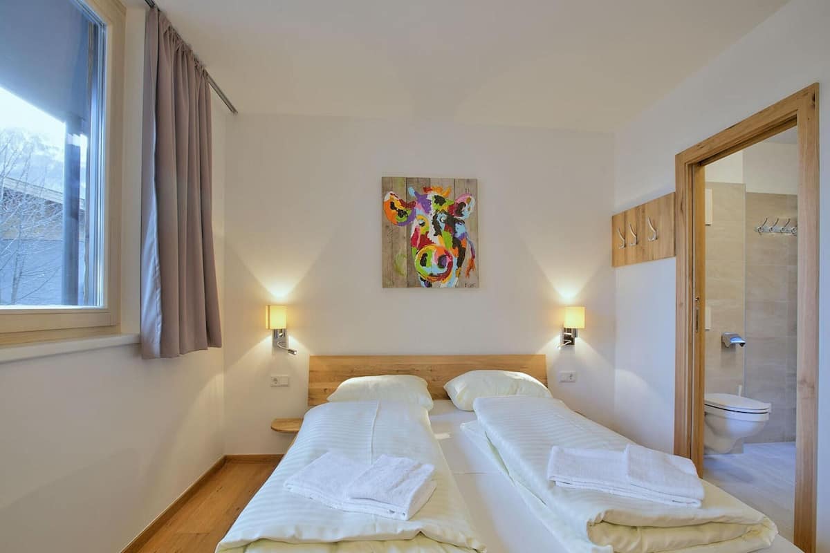 A hotel room with two beds, a large window with curtains, a colorful abstract painting, and a wooden door.