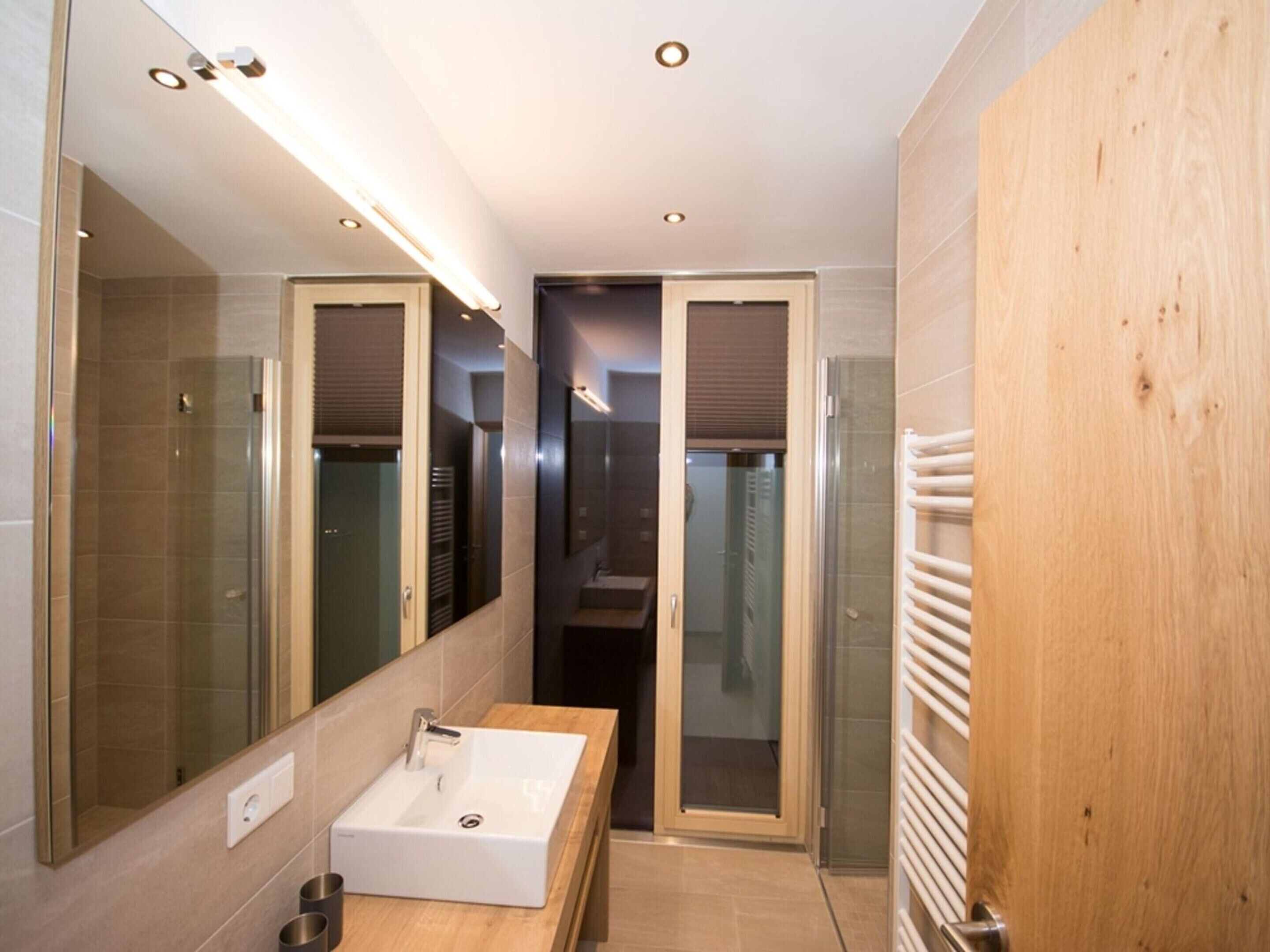 A modern bathroom with a large mirror, a white sink, and a glass shower enclosure.