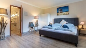 A modern bedroom with a large bed, bedside lamps, a chair, and a view of the bathroom. - Comfortable Holiday Apartment in St. Peter Ording (St. Peter-Ording)