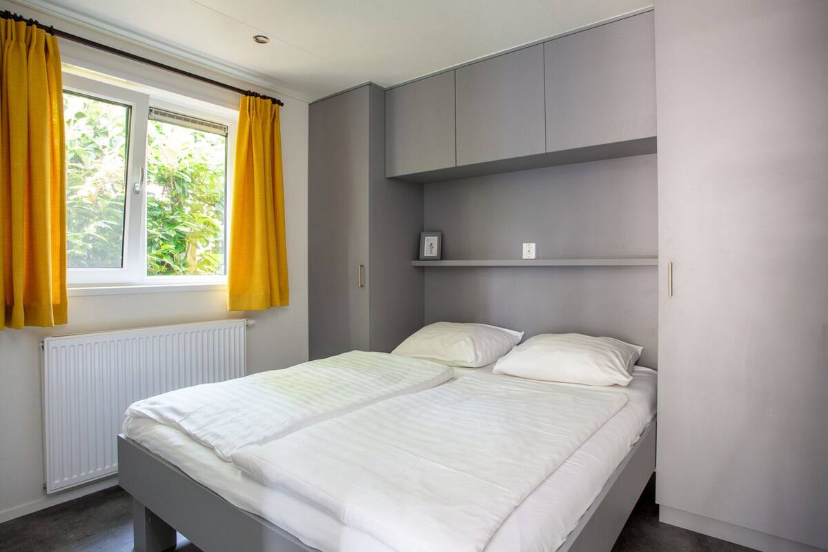 Une chambre à coucher avec un lit, une fenêtre avec des rideaux, un radiateur et une armoire grise.