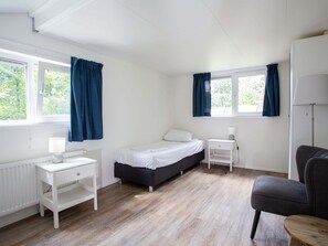 A single bedroom with a bed, a nightstand, a chair, and a window with curtains. - Beautiful House With Covered Terrace, Located in a Holiday Park in Rhenen (Rhenen)