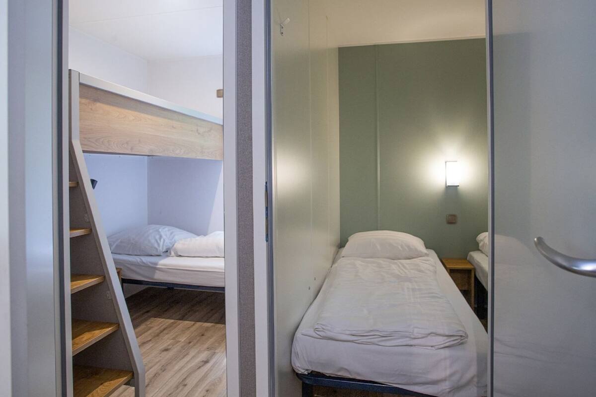Une petite chambre avec un lit superposé et un lit simple, tous deux dotés de draps blancs.