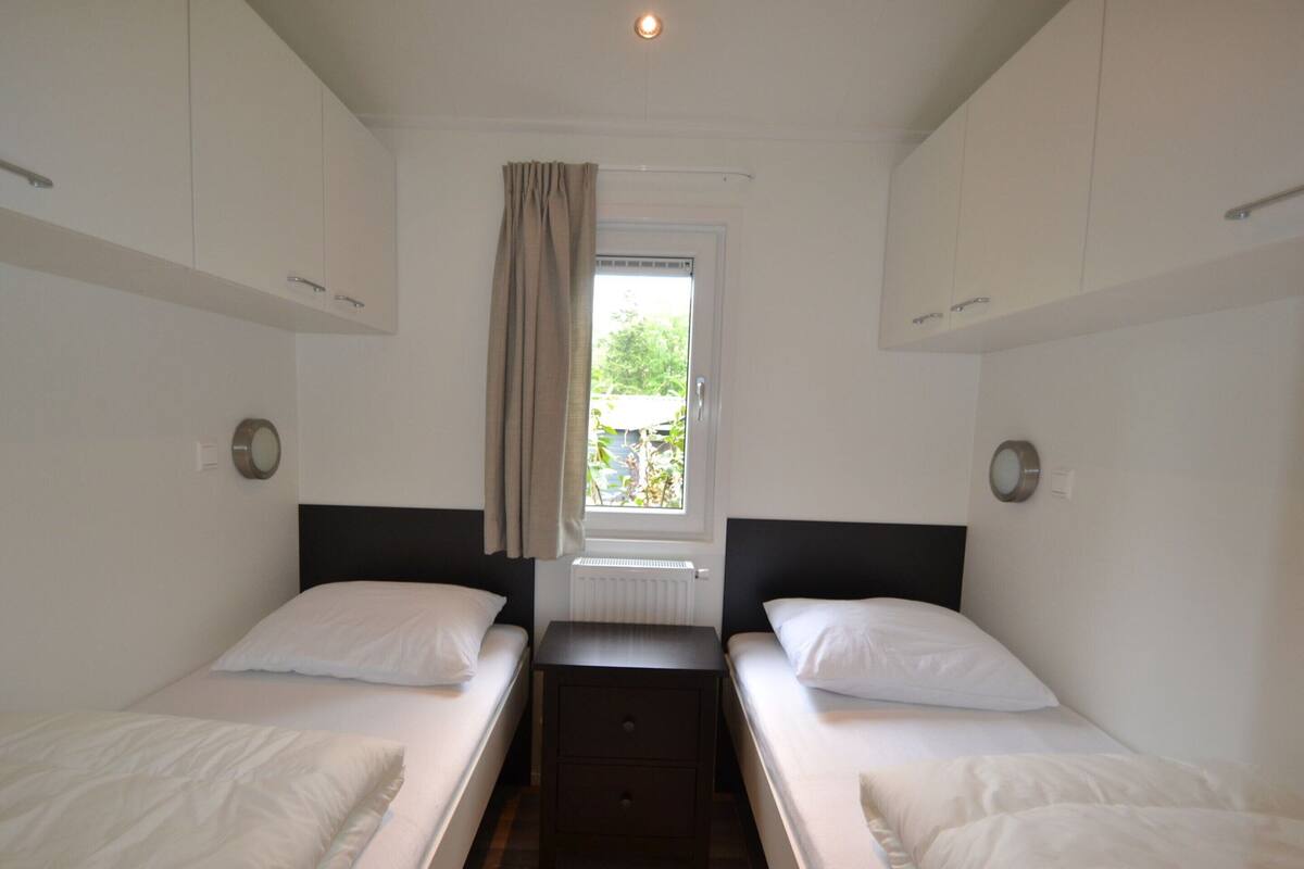 Une chambre double avec deux lits simples, une petite table, une fenêtre avec des rideaux et un radiateur.