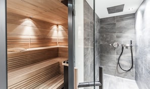 A modern bathroom with a wooden sauna bench and a shower area with grey tiles.